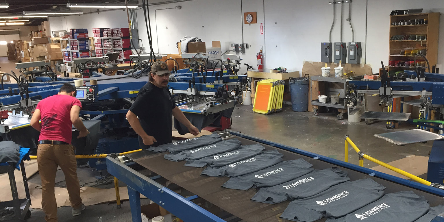 Photograph of screen printing automatic press operators loading shirts onto a conveyor belt to be cured
