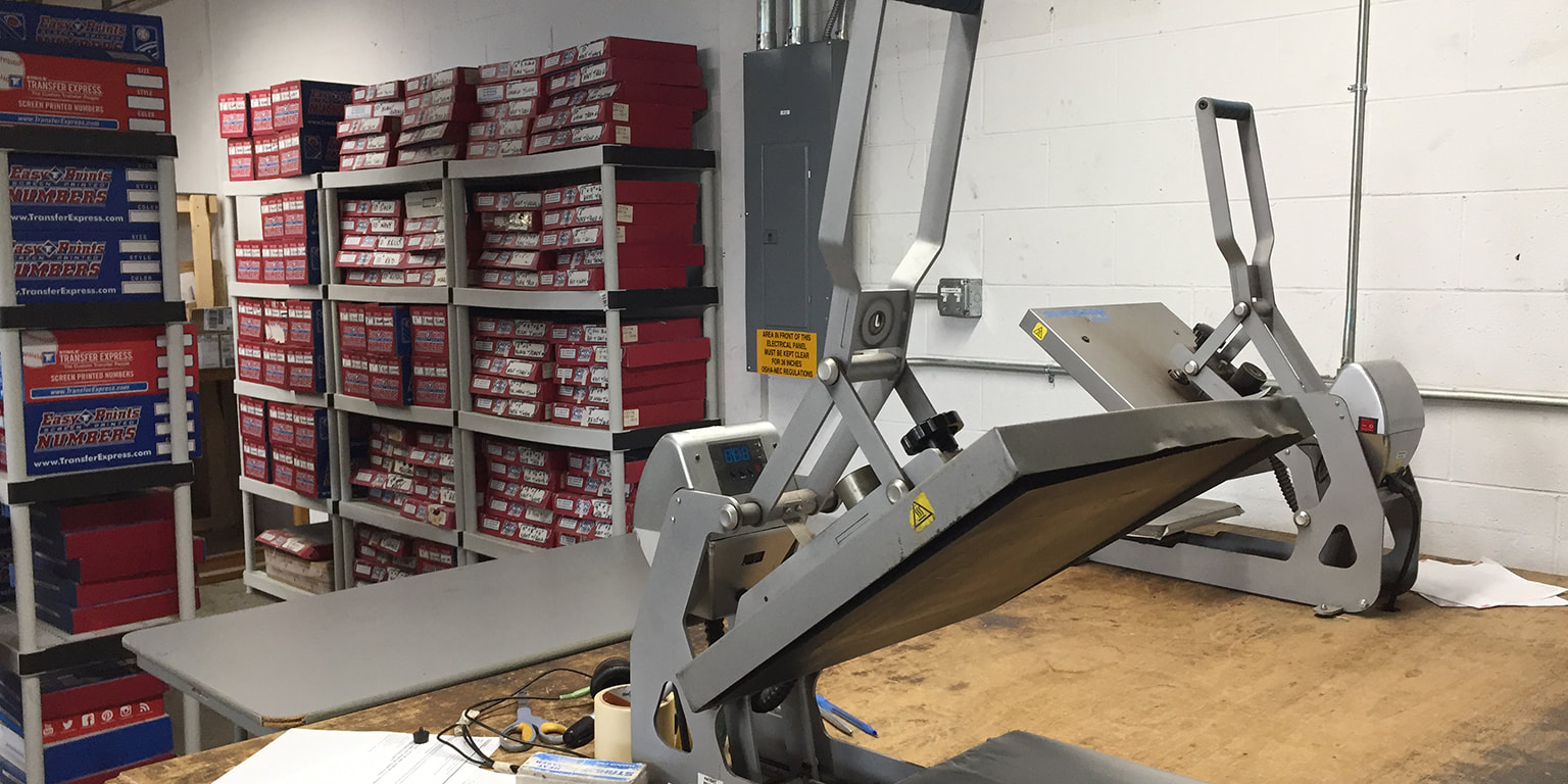 Photograph of heat-seal press machines, with boxes of heat-seal designs behind on shelves
