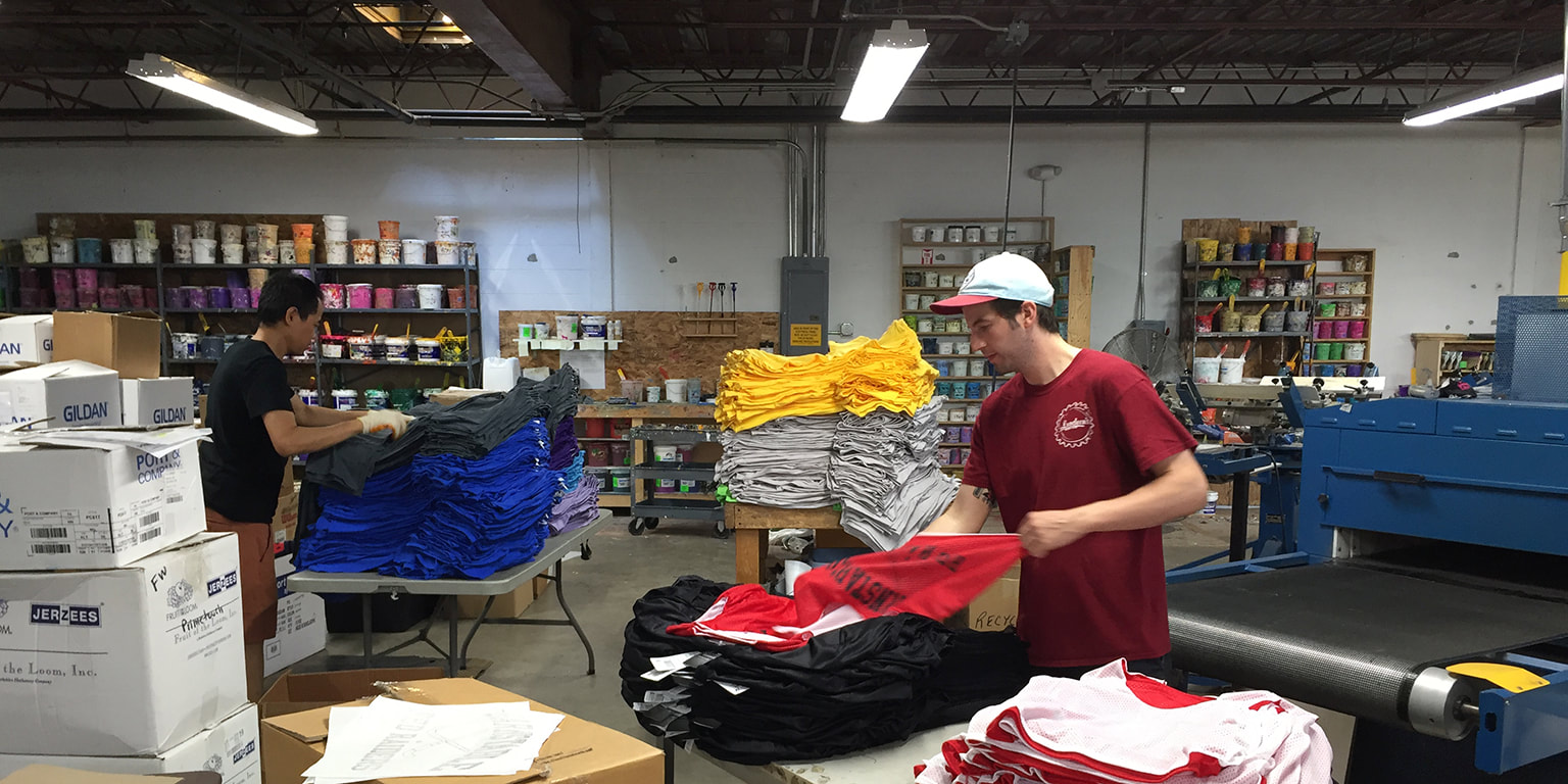 Photograph of a man stacking t-shirts at the end of a conveyor belt